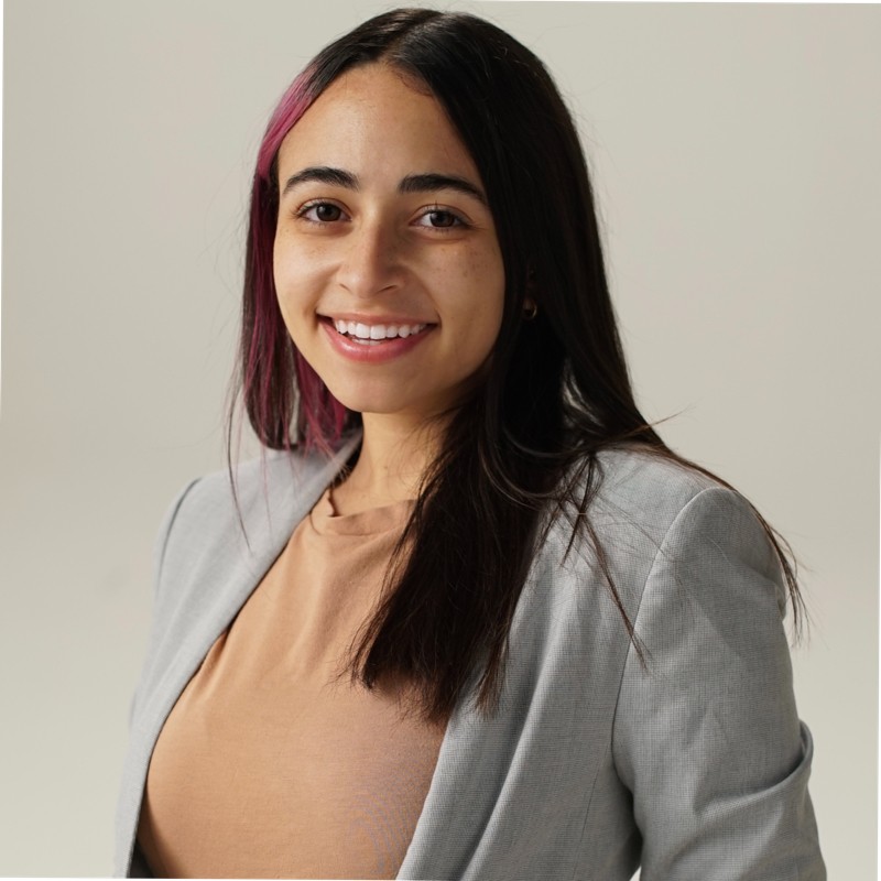 Portrait of a smiling woman in a light gray blazer and beige top, facing the camera against a neutral background.